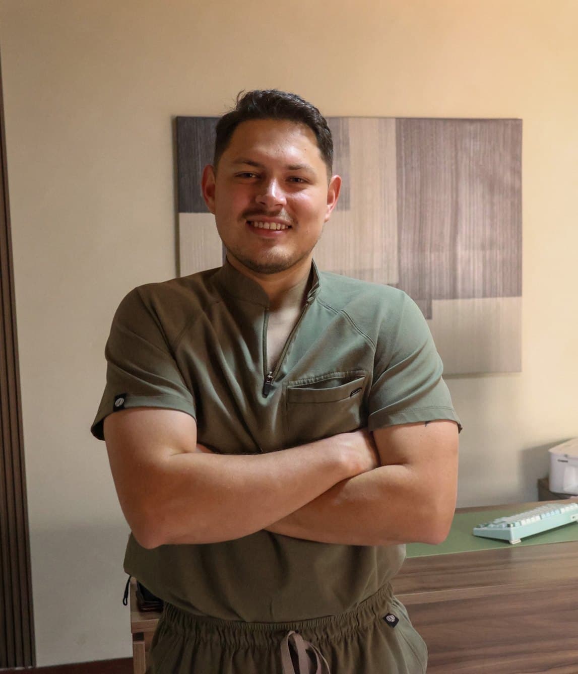 Dr. Brian Amós Zamudio Rodríguez en su consultorio de Saltillo, con filipina verde olivo y los brazos cruzados.